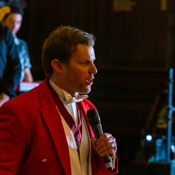 Ross — Professional Toastmaster and Master of Ceremonies in his red coat with microphone